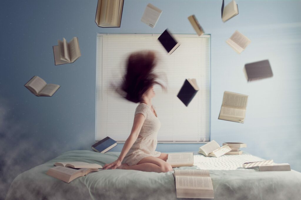 Une femme est  sur un lit, des livres sont jetés en l'air et forment comme une roue autour d'elle